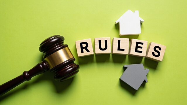 Judge gavel with house icons and wooden blocks spelling rules on a green background for real estate law and property regulation guidance