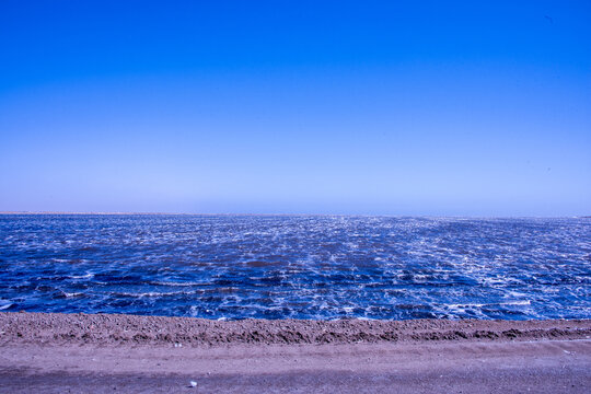 Gentle waves wash over the expansive, sunlit shoreline where the Namib Desert meets the deep blue currents of the Atlantic Ocean at Walvis Bay., Namibia