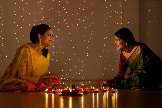 Mother and daughter decorating indoor with diyas on Diwali