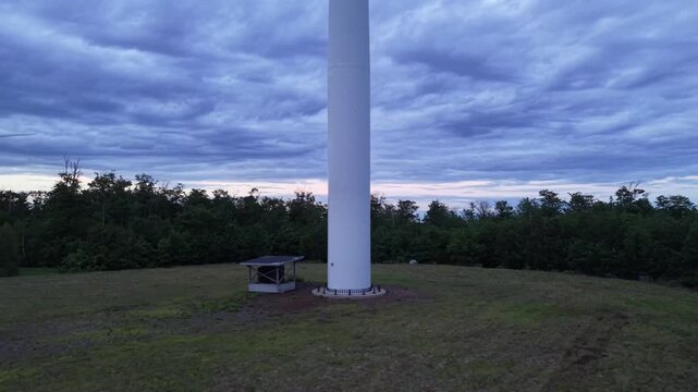 Drone Reveal Of A Wind Turbine Tower Standing Over Rural Landscape Under Dramatic Cloudy Sky At Dusk
