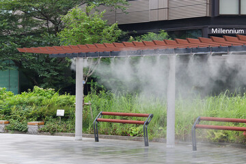 Obraz premium TOKYO, JAPAN - July 16, 2026: Cooling mist emitted from a device over benches in Ginza on a hot summer's day. The Millennium Mitsui Garden Hotel behind it.