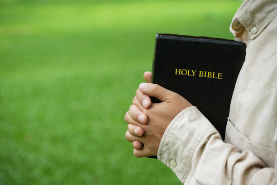 The concept of reading the Bible and praying to God for blessings, living peacefully in nature and spending time with God, with a hand holding a Bible.