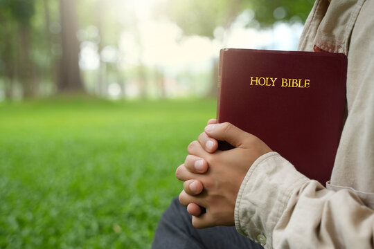The concept of reading the Bible and praying to God for blessings, living peacefully in nature and spending time with God, with a hand holding a Bible.