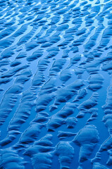Obraz premium Abstract pattern of blue sand ripples created by the tide on a wet beach. Natural texture with flowing lines, ideal as a background or design element.