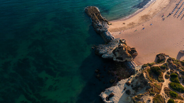 serene rocky coastline with sandy beach and clear blue-green water, aerial perspective from above, relaxing beach getaway scene, natural coastal landscape, clean background.