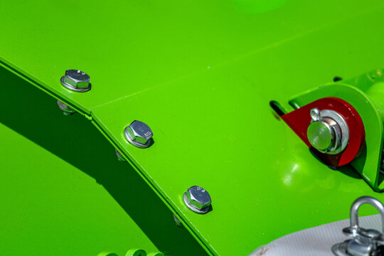 Agricultural disc mower green metal frame bolt joint closeup. Modern farming forage harvester machine steel body construction fastener component with linch pin and technical mechanical details.