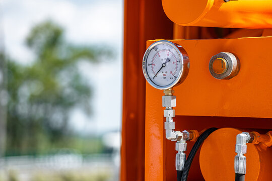 Agricultural machinery hydraulic pressure gauge close up view. Modern farm machine fluid power system monitoring manometer component with steel fittings and technical engineering details.