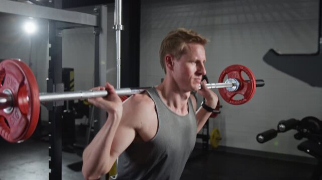 Caucasian man performing barbell squats in gym setting. Clip for fitness center promotions, athletic training advertisements, and healthy lifestyle campaigns