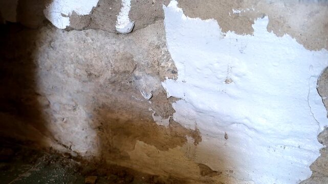 Professional builder carefully levels an old uneven concrete wall with white putty using a large metal spatula. This video close-up details the process of home repair, renovation, surface preparation,