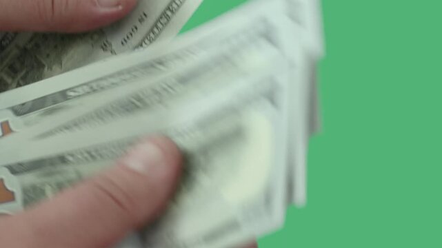 Counting hundred dollar bills carefully in hands against a vibrant green background in bright light