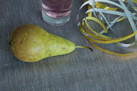 Pear placed on a gray surface next to a glass of water and colorful ribbons