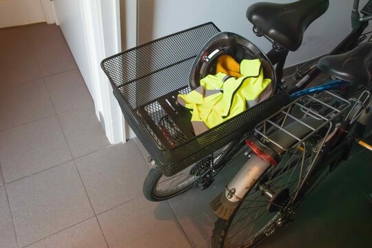 Bike with a basket holding a helmet and a yellow jacket in a hallway near a door