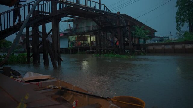 Small boat by water canal during rainfall near wooden pedestrian bridge, Rain falling over channel houses and bridge in Lat Krabang 4k
