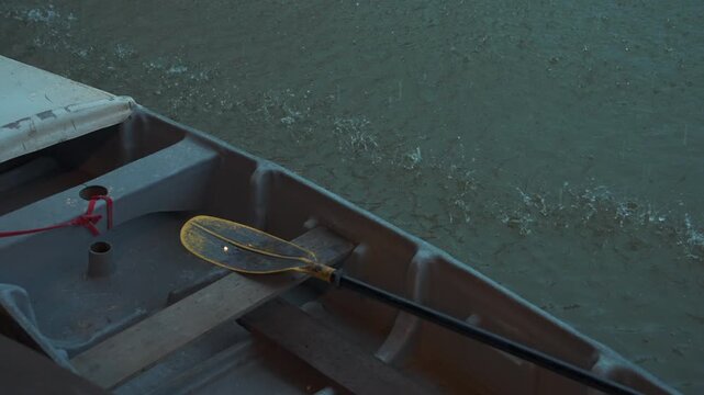 Small boat with paddle during rainfall on canal water, Raindrops splashing around rowing boat with wooden seat and paddle on water surface 4k