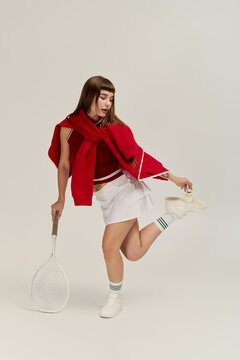 Stylish young woman showcasing tennis fashion in a grey studio setting