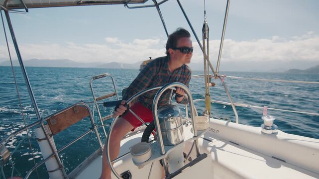 Young man sailor sailing alone the small sailing boat in the fresh sea during nice sunny day. Sailor enjoys the wind. Confident sailor steers the sail boat