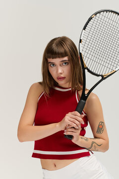 Stylish young woman embodies retro tennis vibes in grey studio