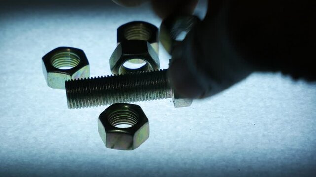 Hand Placing Metal Hex Nuts Around a Bolt on Textured Surface