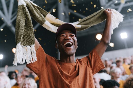 Excited fan cheering with scarf and confetti at stadium crowd for sports event banner and celebration background