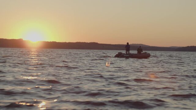 Two men fishing from the inflatable boat on the river at sunset and cast lures