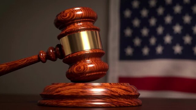 A wooden gavel rests on a sound block in front of a blurred American flag, symbolizing justice and law.