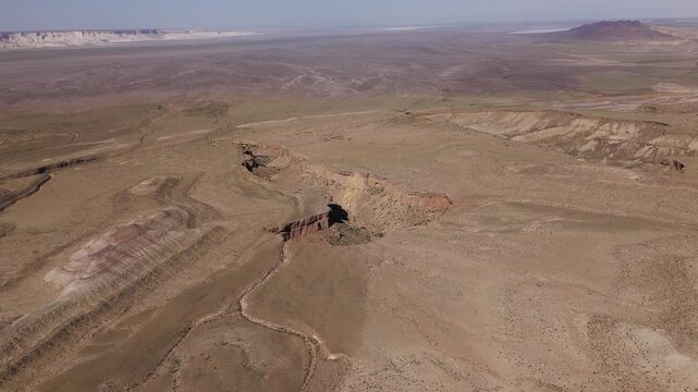 An epic cinematic drone shot revealing a massive earth sinkhole and dramatic canyon system within the vast desert plains of the Karynzharyk depression in Mangystau, Kazakhstan
