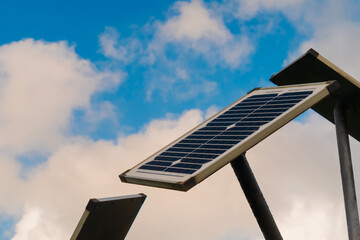 Naklejka premium Solar panels against white clouds in the blue sky - close up view. Renewable energy, alternative source of electricity, technology, and ecological concept