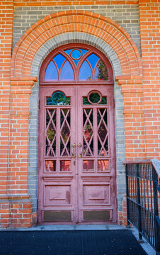 An old wooden door with a metal handle and hardware. A bright sunny day, a red brick building.