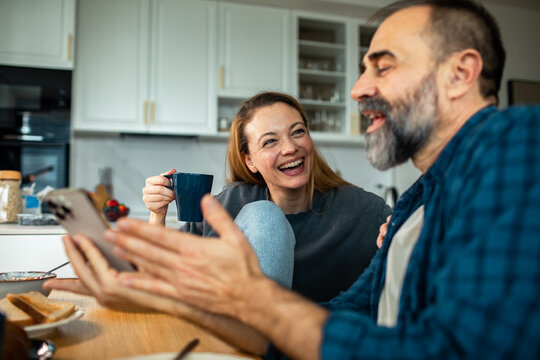 Happy couple laughing over coffee in home kitchen