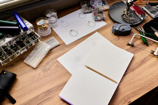 Top view of jewelry designer workspace showing sketching ring concepts beside tools and materials. Supporting artisan branding, handmade product marketing, small business content