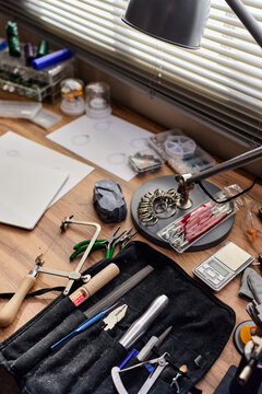 Vertical close up of jewelry making tools and gemstone resting on workbench, supporting artisan crafting and product development. Useful for handmade business, ecommerce, workshop branding