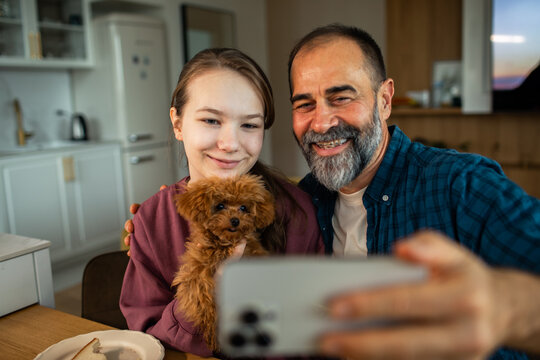 Father and daughter taking selfie with toy poodle puppy in home kitchen