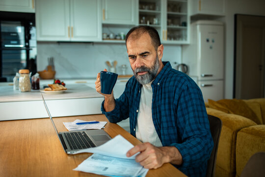 Middle-aged man reviewing household bills at kitchen table