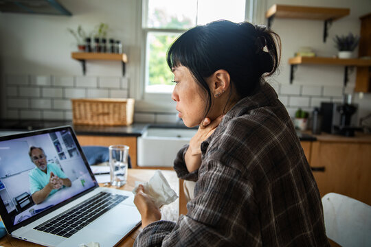 Sick woman consulting doctor via telehealth at home kitchen