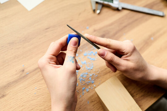 Close up of young adult woman hands filing blue wax block over table, creating custom jewelry in workshop. Useful for education, creativity, learning support