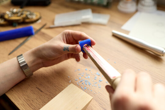 Close up of young adult woman carving blue wax block with file at jeweler workbench, shaping handmade accessory prototype. Ideal for artisan craft, small business, product design marketing