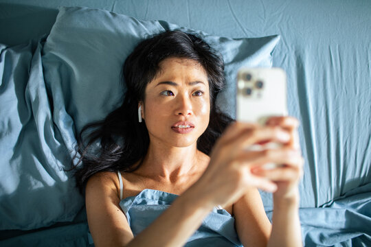 Woman lying in bed video calling on smartphone at home