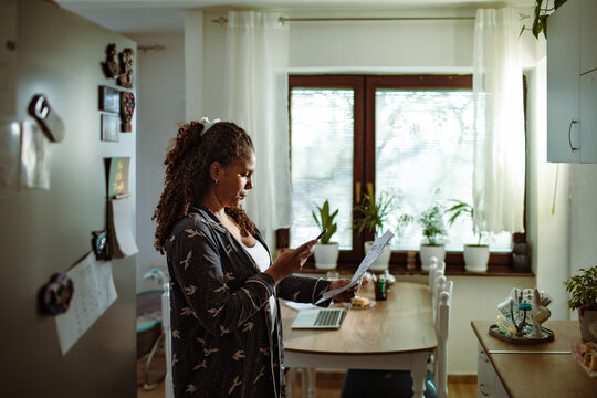 Woman scanning household bill with smartphone in kitchen