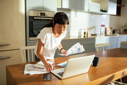 Woman paying bills on laptop in home kitchen