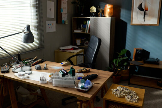 Wide shot of jeweler workspace displaying tools, gemstones, metal pieces, and unfinished accessories on desk, suggesting handmade production. Ideal for artisan branding and craft business marketing