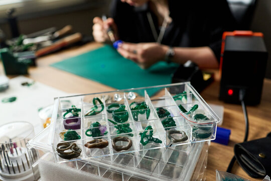 Close up of young adult woman repairing 3D printed jewelry pieces at workbench, organizing prototypes for product development and handmade accessory marketing