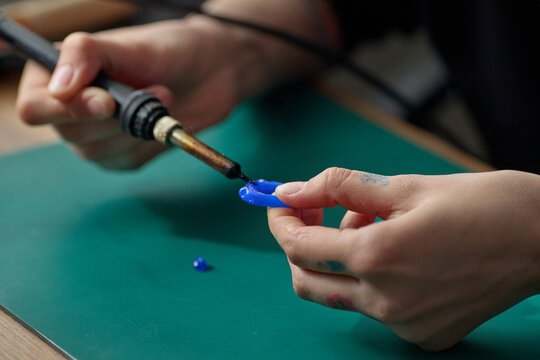 Close up of young adult hands soldering blue plastic component on workbench, assembling craft project with precision. Useful for maker education, DIY workshop, repair training marketing