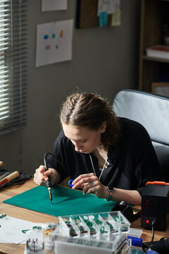 Vertical shot of young adult Caucasian woman soldering ring mold at workbench, assembling prototype for product development. Ideal for STEM training, maker culture, tech education