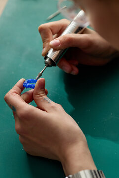 Vertical shot of young adult hands shaping blue prototype with rotary tool, refining product model for design process. Useful for product development, maker culture, innovation marketing