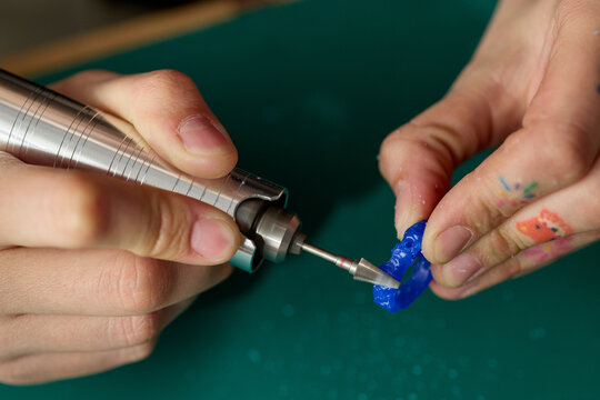 Close up of adult hands shaping blue model with rotary tool, demonstrating precision crafting and prototyping. Useful for maker education, product design, engineering process content