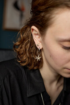 Vertical shot of young adult Caucasian woman lowering gaze in close up, showing ear piercings and jewelry styling. Suitable for fashion retail, beauty branding, accessory marketing