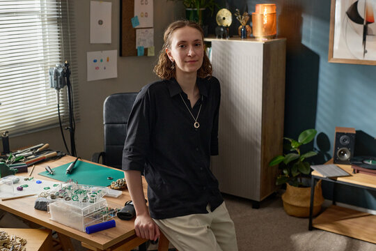 Portrait of young adult Caucasian woman standing by worktable, creating handmade jewelry in studio and looking at camera. Ideal for artisan business, creative entrepreneurship marketing