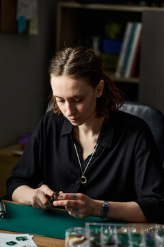 Vertical shot of young adult Caucasian woman crafting small object at worktable, focusing on handmade production and creative process. Useful for artisan business, maker marketing