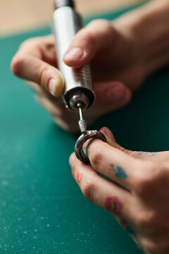 Vertical close up shot of young adult craftsperson polishing ring with rotary tool, refining handmade jewelry for production. Ideal for artisan branding, ecommerce, workshop promotion