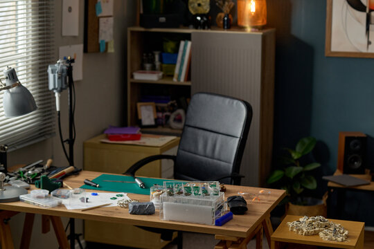Wide shot of empty craft studio workspace displaying jewelry making tools and unfinished pieces on desk, suggesting artisan production. Suitable for small business, handmade product marketing